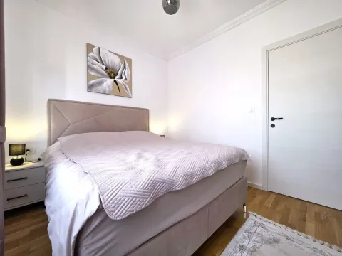 Svjetla spavaća soba sa bračnim krevetom, noćnim stočićem i slikom na zidu. - image 12