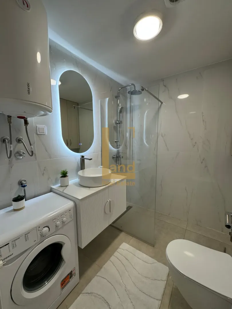 Moderne kupatilo sa tuš kabinom, umivaonikom i veš mašinom.