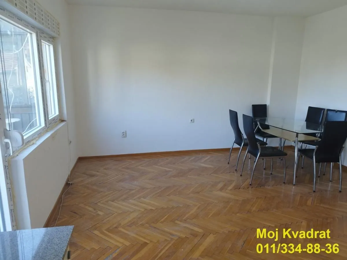 Dining area with a glass table and black chairs in a room with parquet flooring.