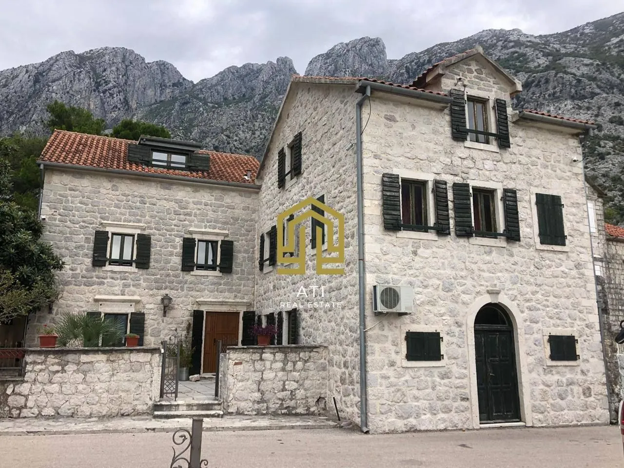 Eksterijer tradicionalne kamene kuće sa planinskim pejzažem u pozadini.