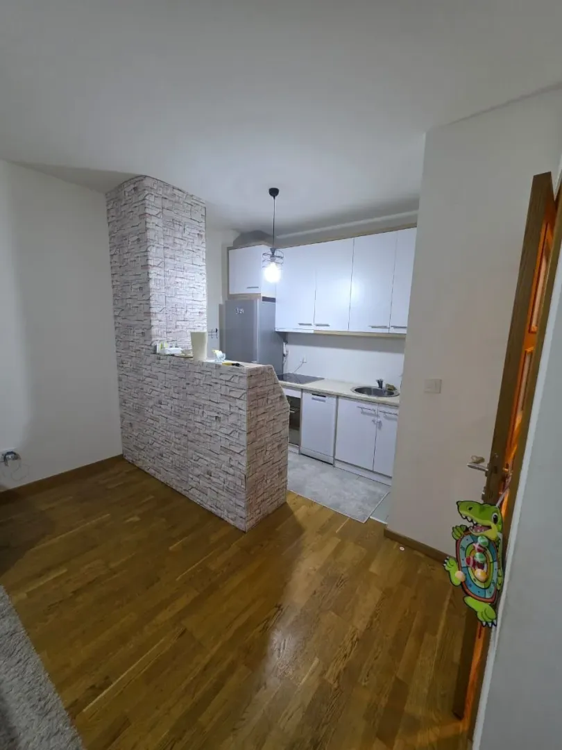Manja kuhinja sa bijelim elementima i šankom obloženim tapetama koje imitiraju ciglu.
