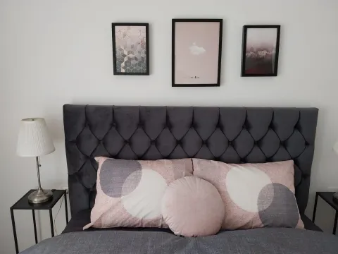 A neatly made bed with a grey headboard and decorative pillows. - image 13