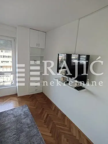 Living room with a TV, shelving, and parquet flooring.