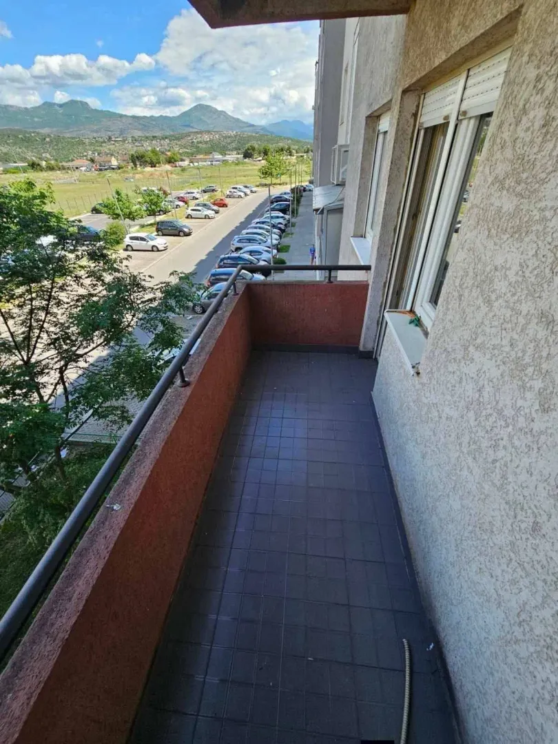 Dugi balkon sa podnim pločicama i pogledom na parking i okolne planine.