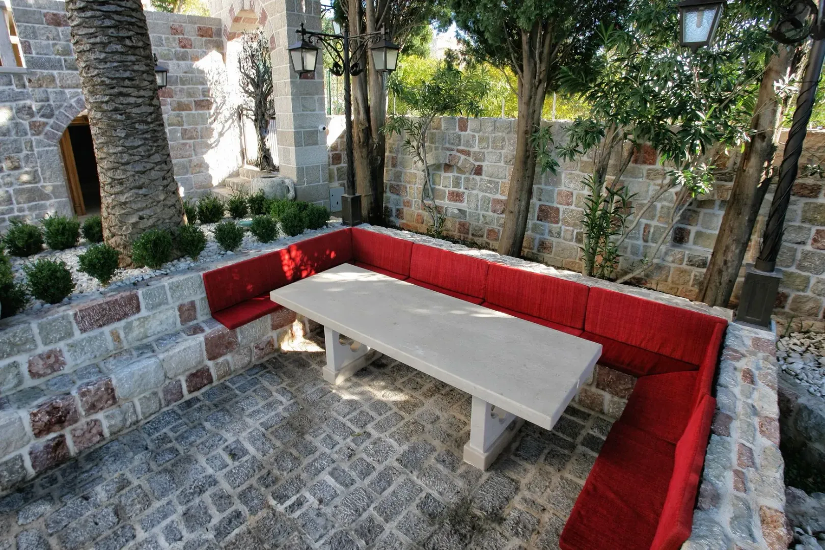 Stone-paved patio featuring a table and a built-in bench with red cushions.