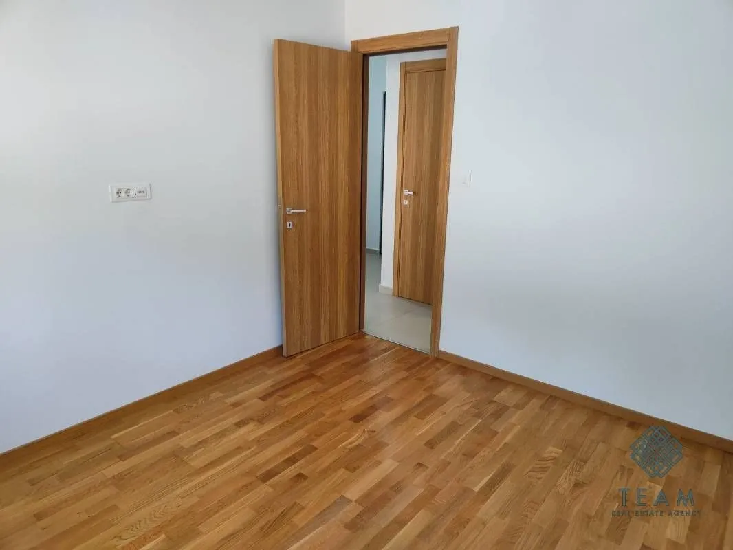 Prazna soba sa drvenim parketom i otvorenim drvenim vratima.