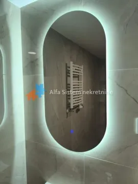 Close-up of the bathroom featuring a large oval LED backlit mirror and ceramic wall tiles. - image 5
