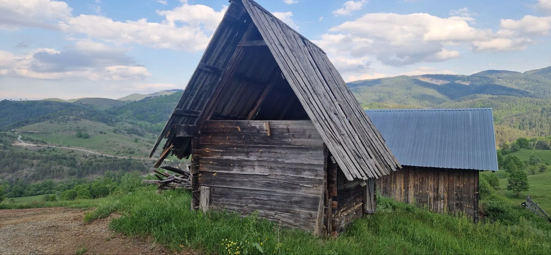 Stare drvene kolibe na brdu okružene prirodom i planinskim pejzažem.
