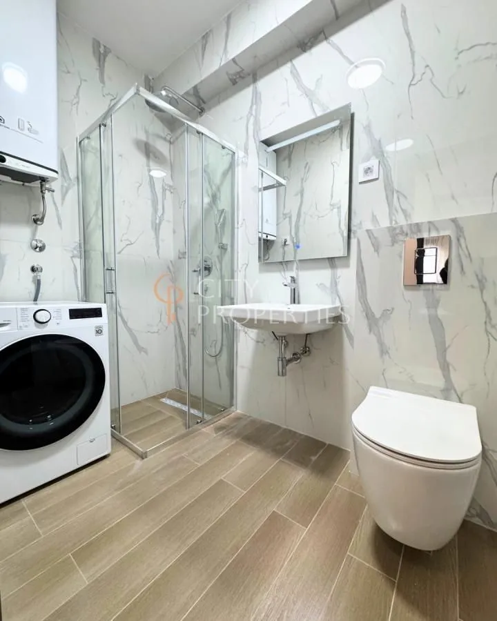 Moderne kupatilo sa tuš kabinom, umivaonikom, WC šoljom i mašinom za veš.