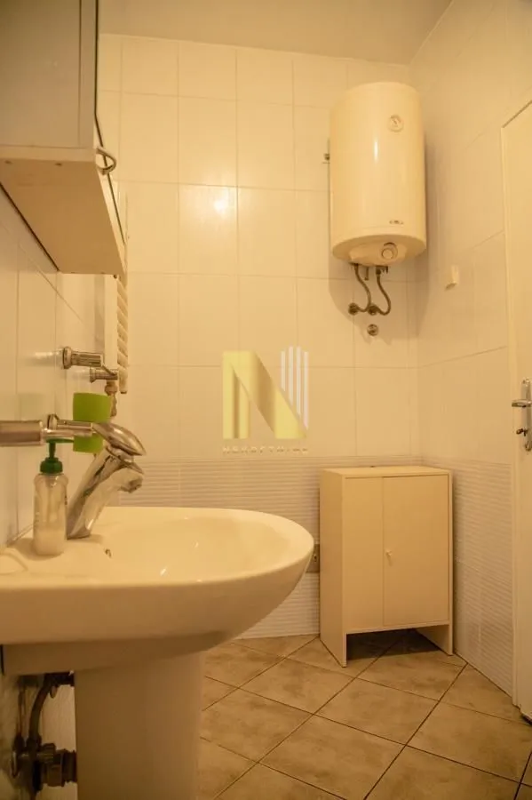 Kupatilo opremljeno umivaonikom, bojlerom i pločicama na zidovima.