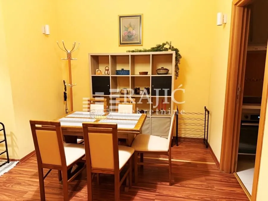 Dining area with a wooden table, chairs, and shelving unit in an apartment.