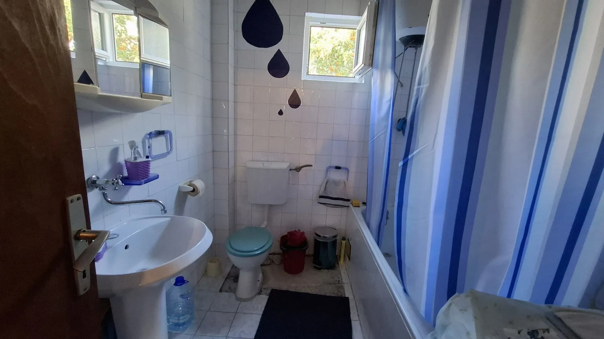 Manje kupatilo sa umivaonikom, wc šoljom i kadom sa zavesom.