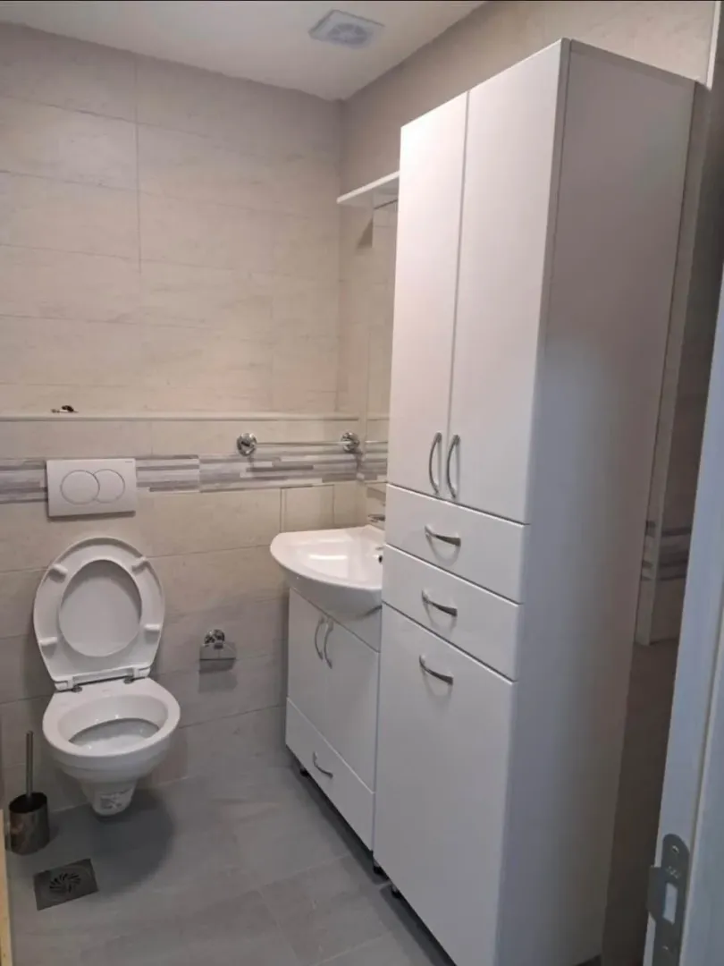 Kupatilo opremljeno toaletom, umivaonikom i bijelim ormarićem.