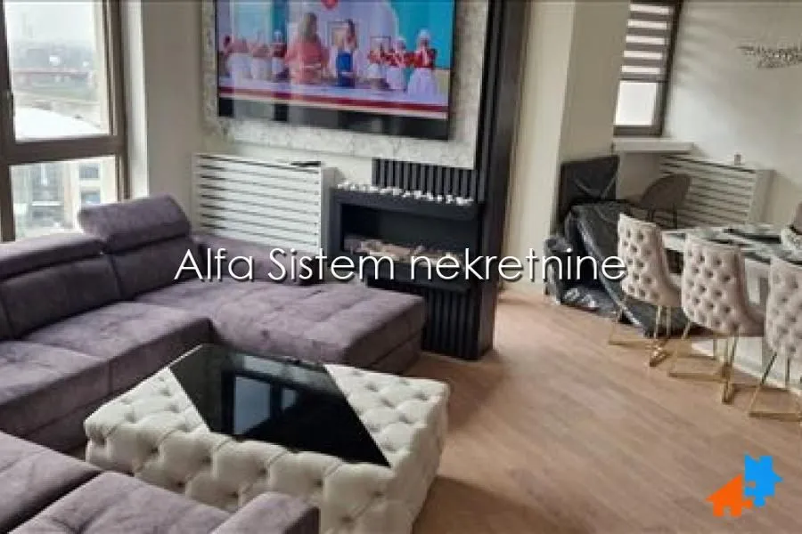 Dnevna soba sa ugaonom garniturom, televizorom i trpezarijom u pozadini.