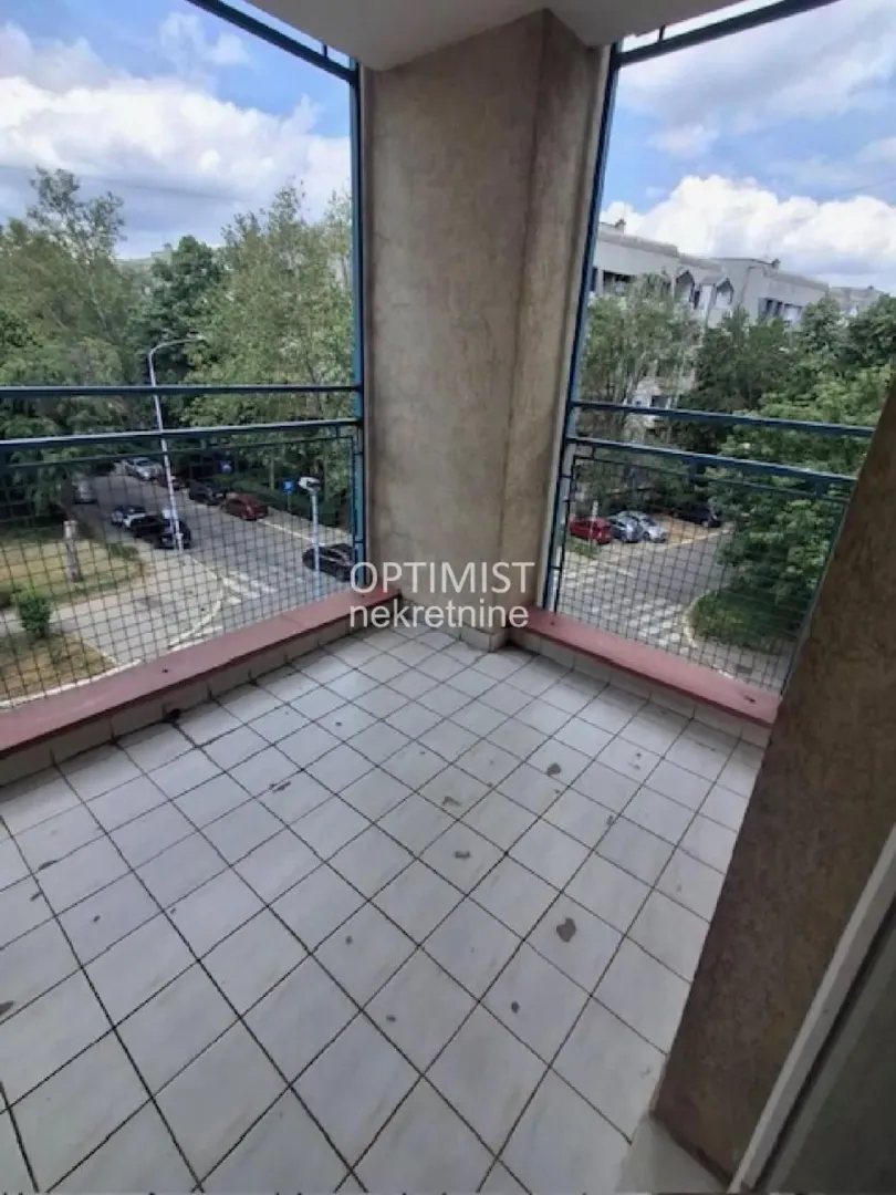 Natkriveni balkon sa popločanim podom i metalnom ogradom i pogledom na ulicu.