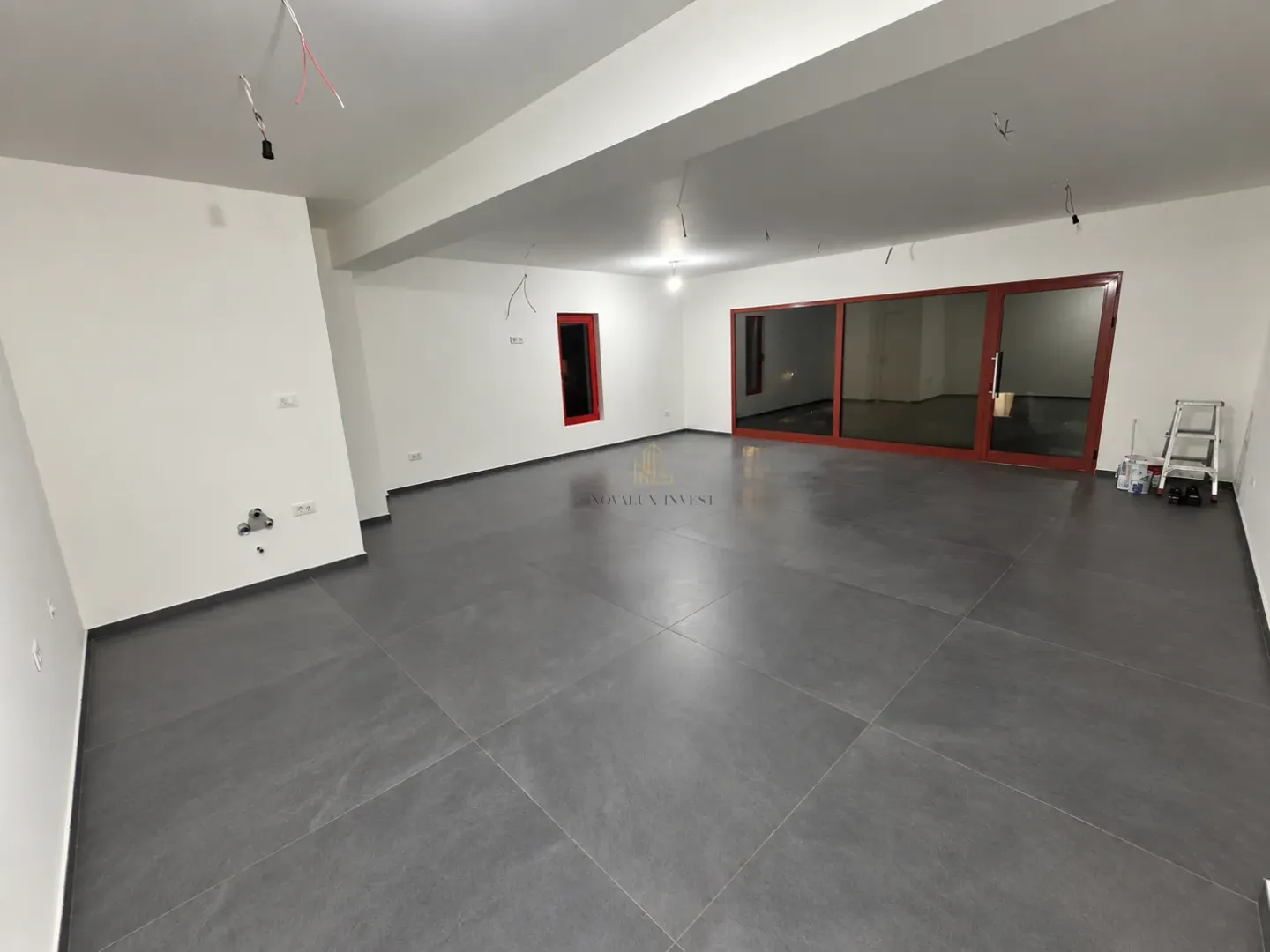 Empty unfinished room with grey floor tiles and large glass openings.