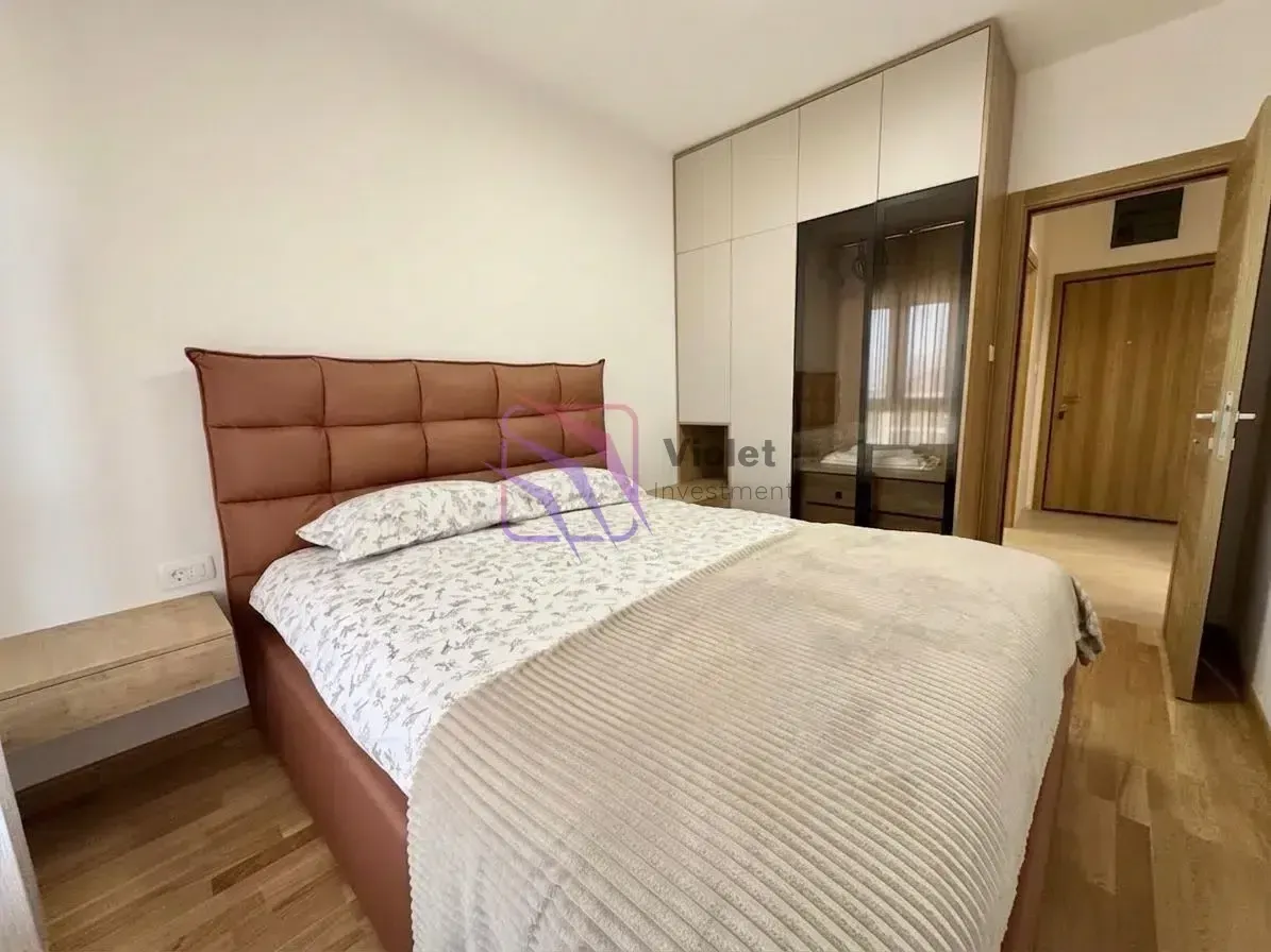 Namještena spavaća soba sa bračnim krevetom, ugradnim plakarom i drvenim podom.