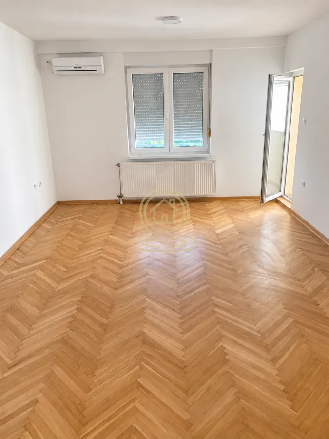 Prazna soba sa parketom, klima uređajem i izlazom na terasu.