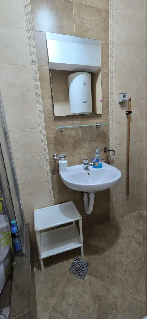 Kupatilo sa umivaonikom, ogledalom i pločicama u neutralnim tonovima.