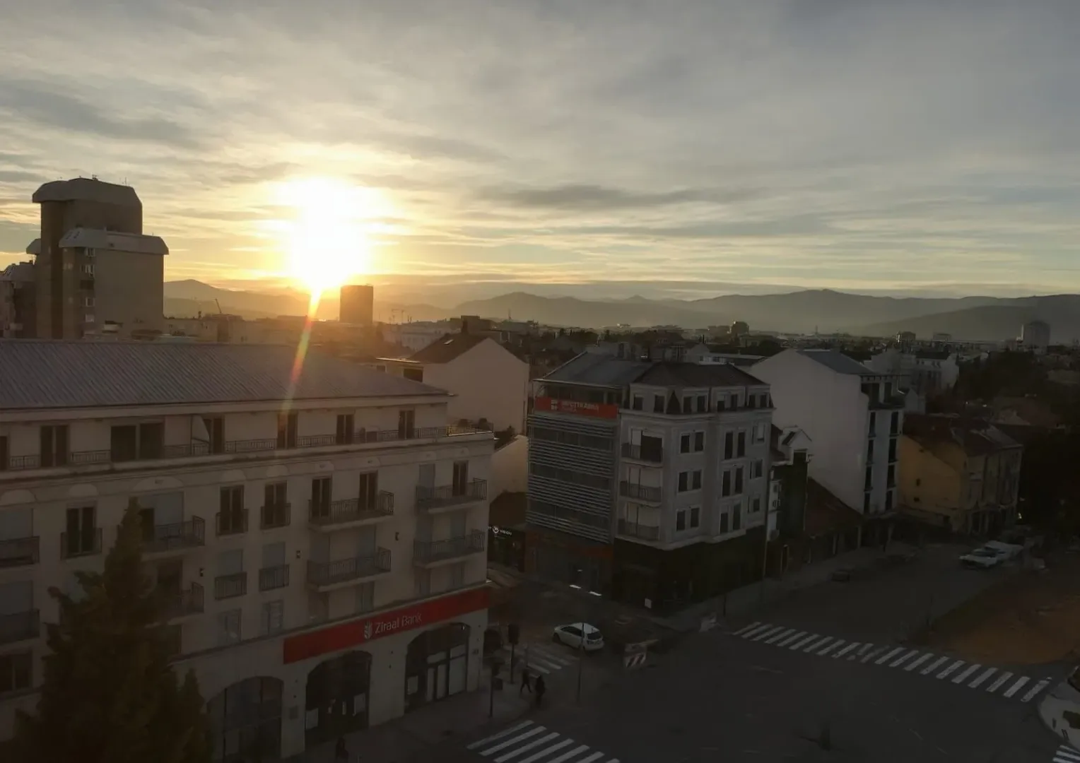 Pogled na grad sa panoramskim prikazom okolnih zgrada i planina u pozadini tokom zalaska sunca.