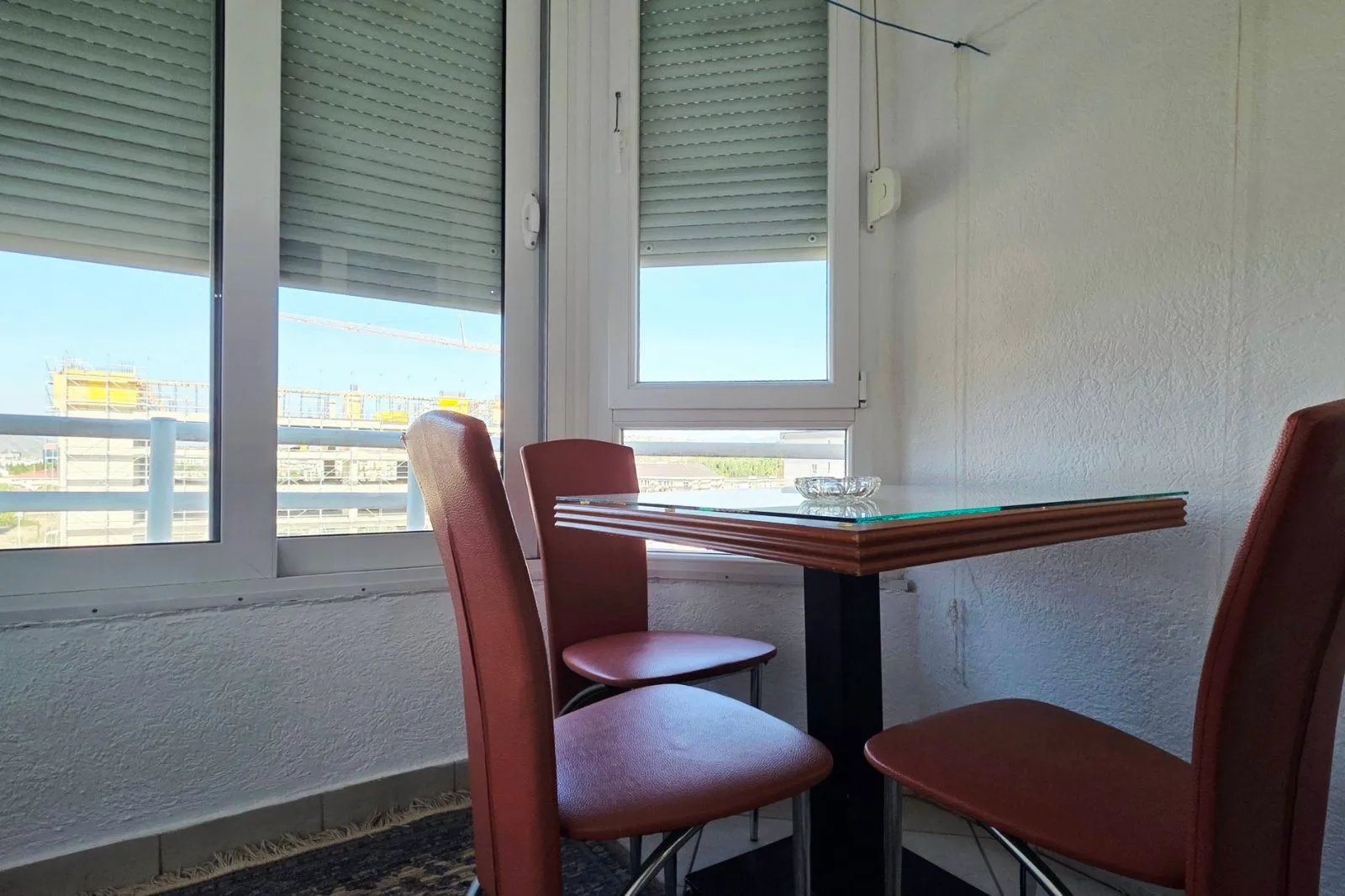 Enclosed balcony with a dining table and red chairs by the window.