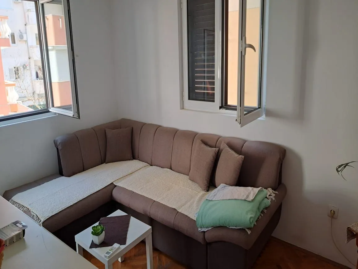 Living room with a sectional sofa and windows overlooking surrounding buildings.