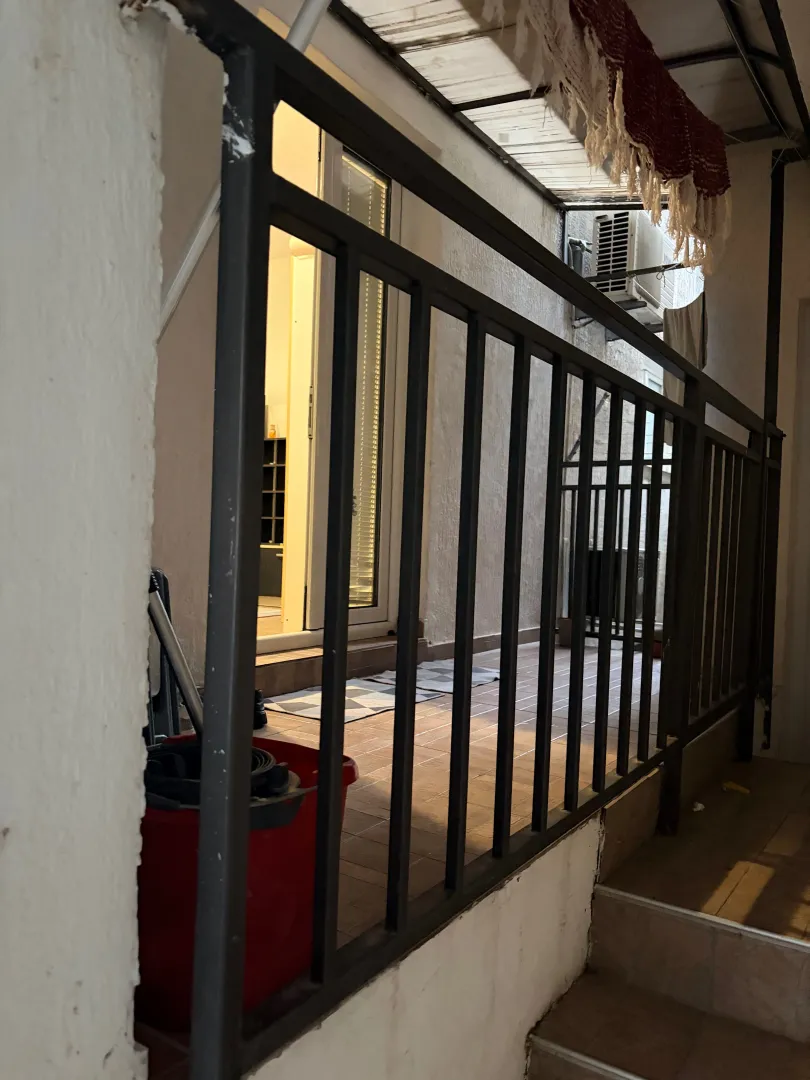 Manji natkriveni balkon sa metalnom ogradom i pogledom na unutrašnji dio zgrade.