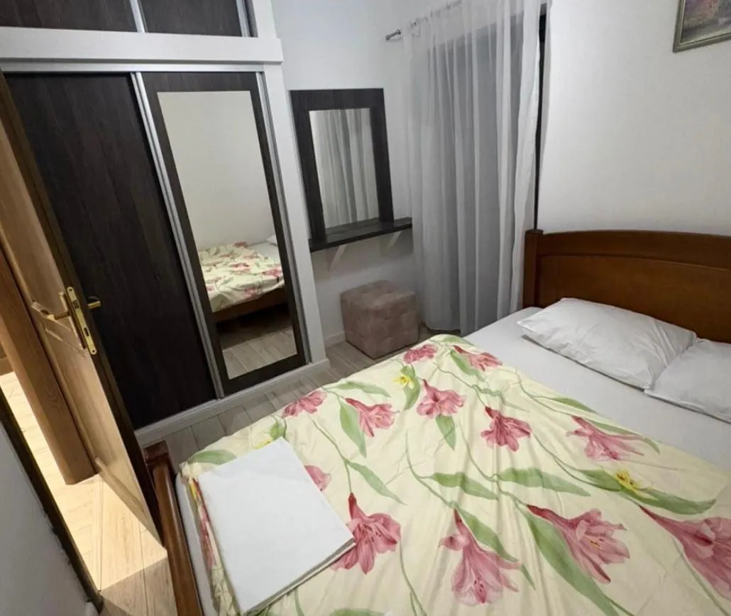 Furnished bedroom with a double bed, mirrored wardrobe, and a window.