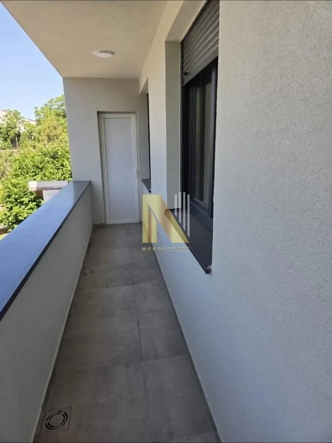 Dugački popločani balkon sa prozorom i vratima koja vode u stan.