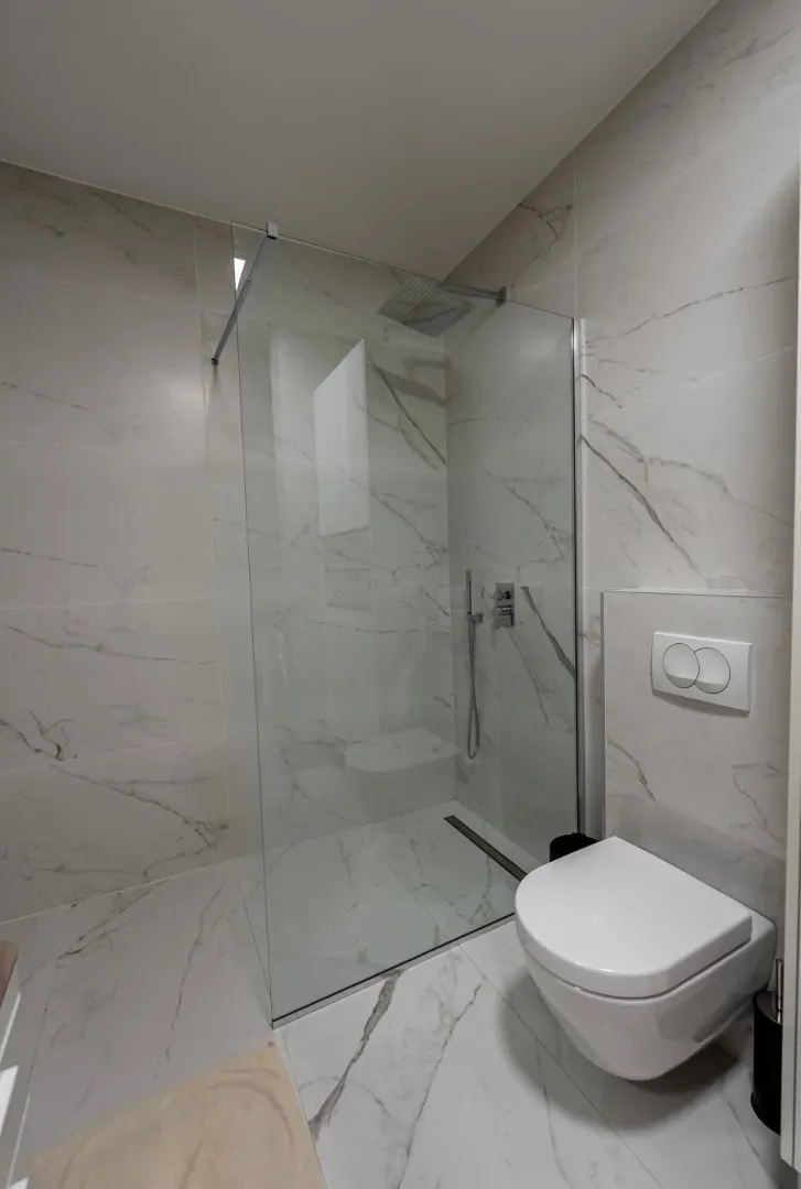 Modern bathroom with a walk-in shower and a wall-hung toilet, tiled with marble-patterned tiles.