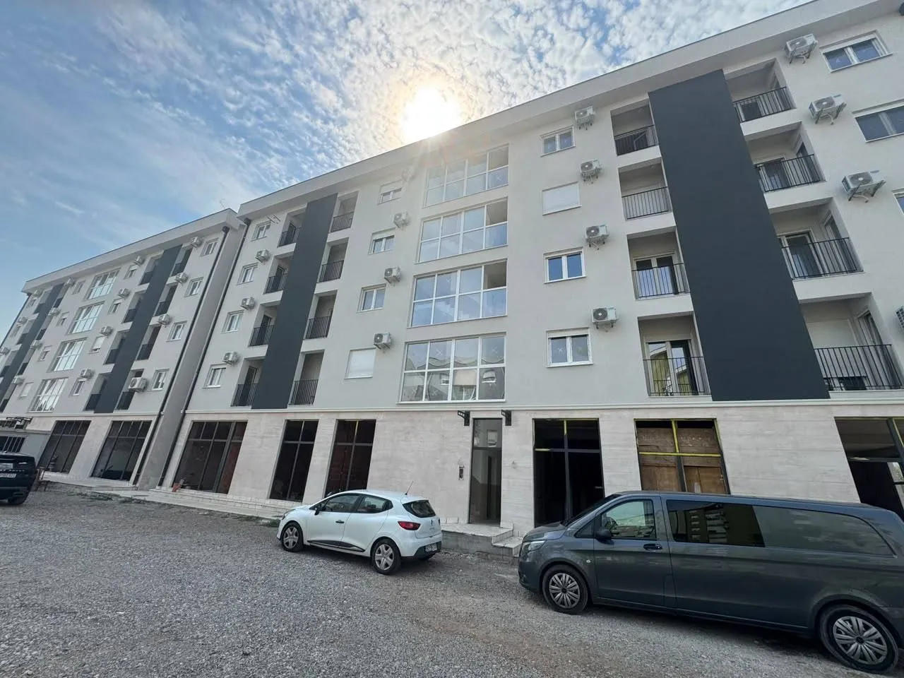 Exterior view of a modern residential building with balconies and cars in the yard.