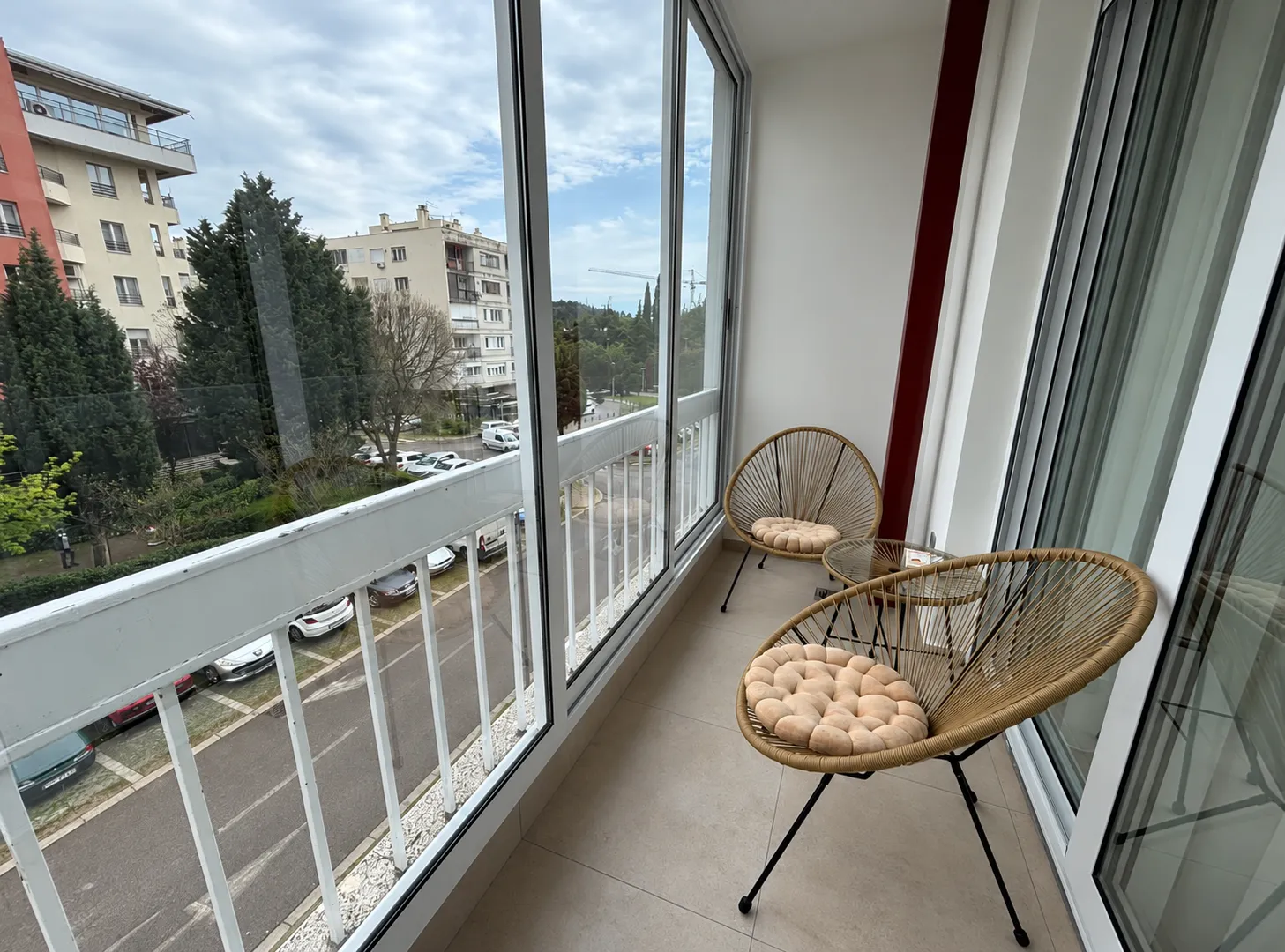 Zastakljeni balkon sa garniturom za sjedenje i pogledom na ulicu.