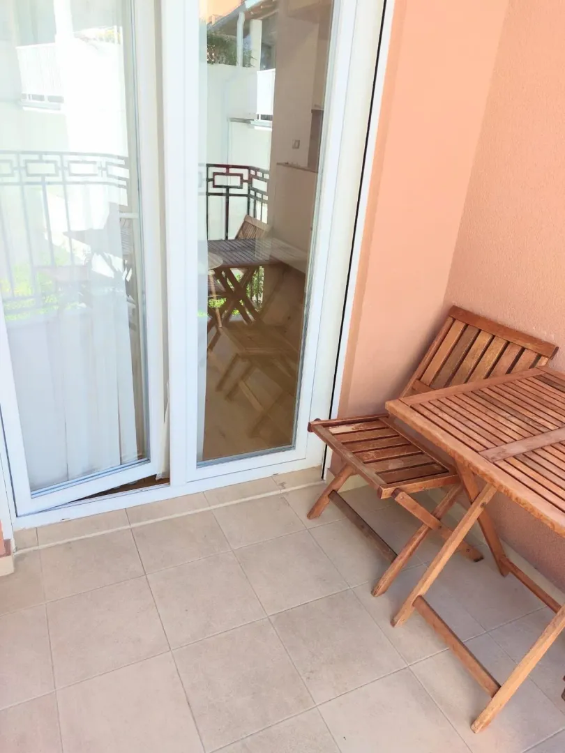 Small wooden table with chairs on a tiled balcony with glass balcony doors.