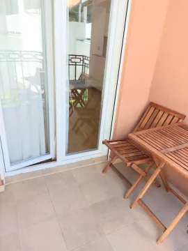 Small wooden table with chairs on a tiled balcony with glass balcony doors. - image 17