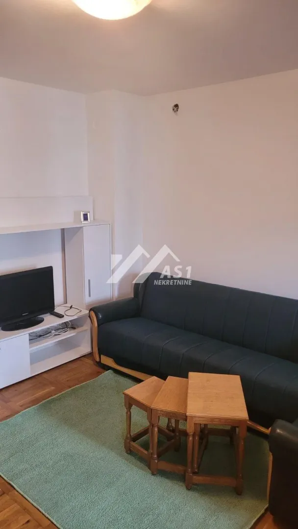 Dnevna soba sa garniturom za sedenje, televizorom i malim stočićem.
