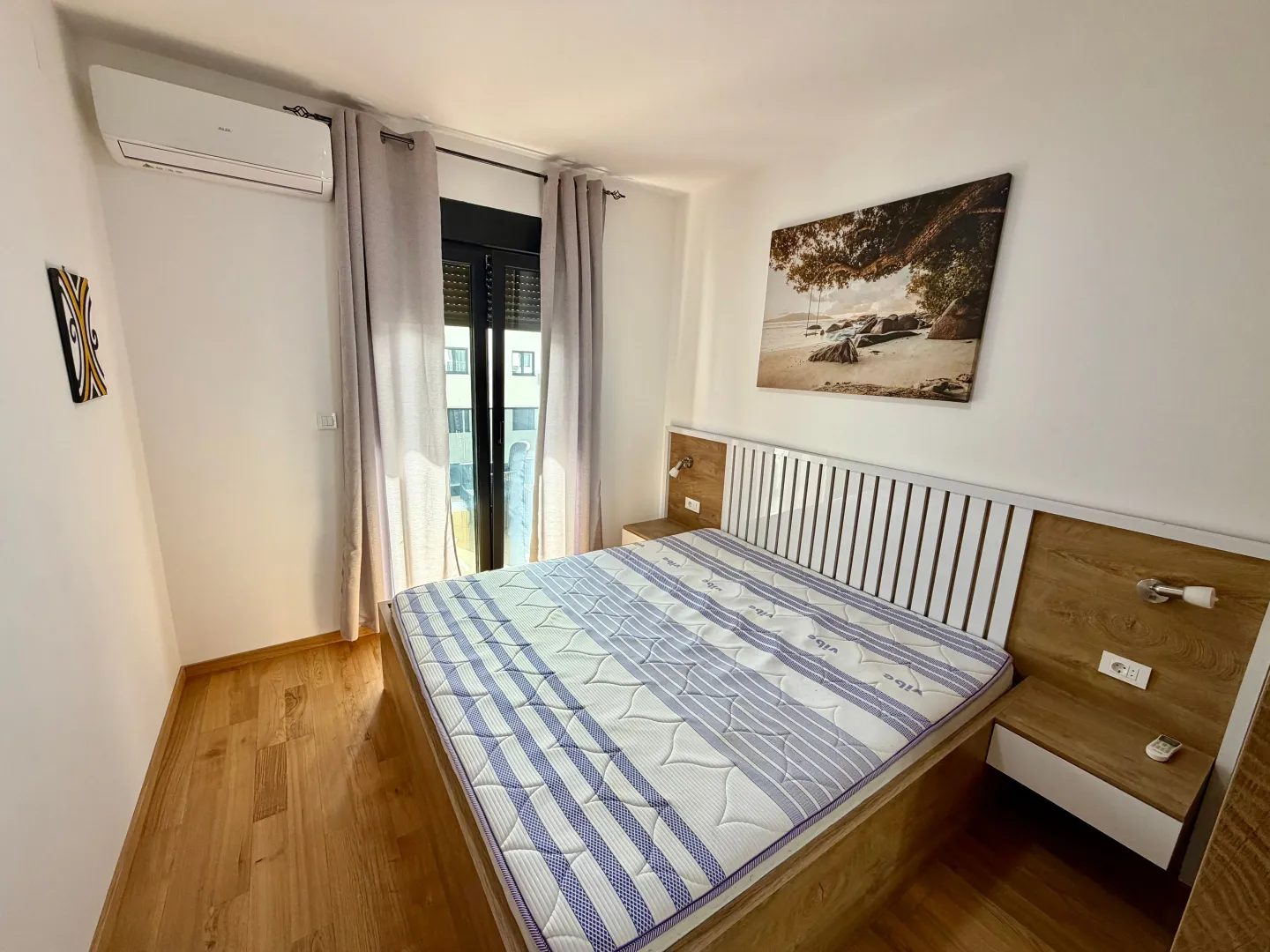 Bright bedroom with a double bed, wooden floor and air conditioning.