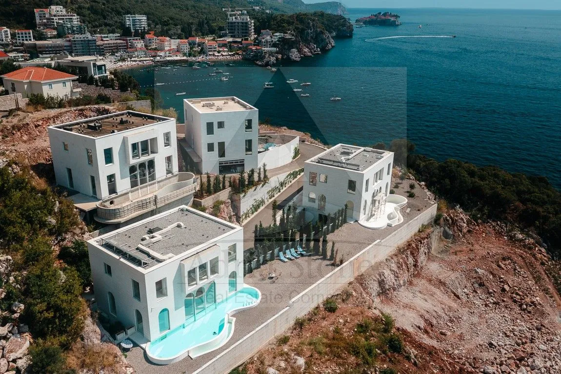 Pogled iz vazduha na kompleks modernih vila sa bazenima na obali mora.