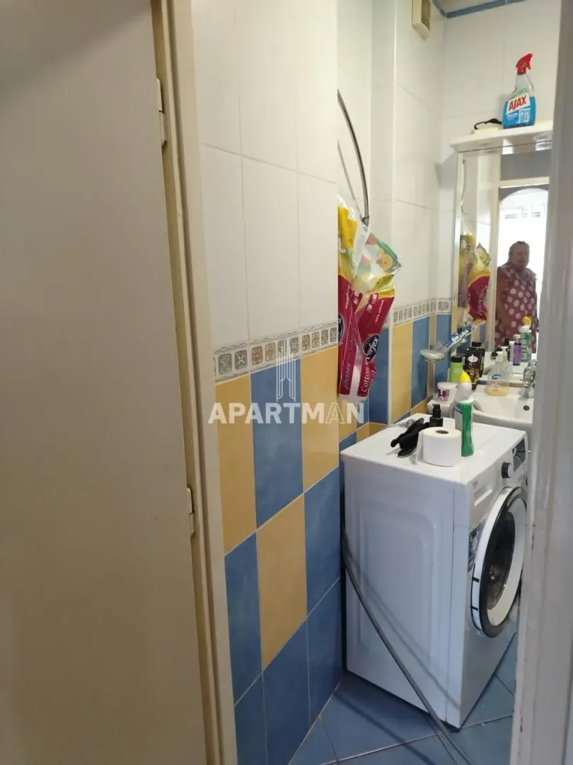 Manje kupatilo sa pločicama u plavoj i žutoj boji, umivaonikom i veš mašinom.