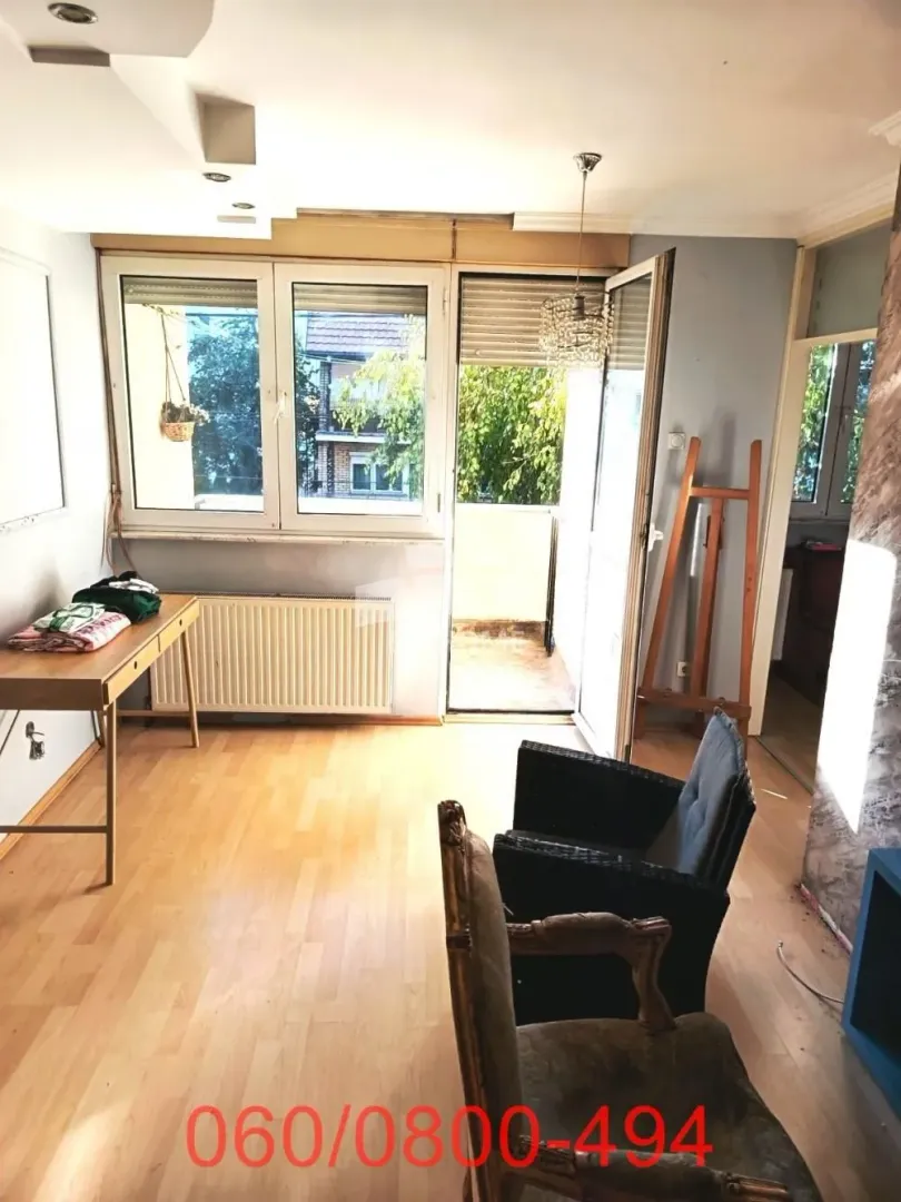 Dnevna soba sa izlazom na balkon i drvenim podom.