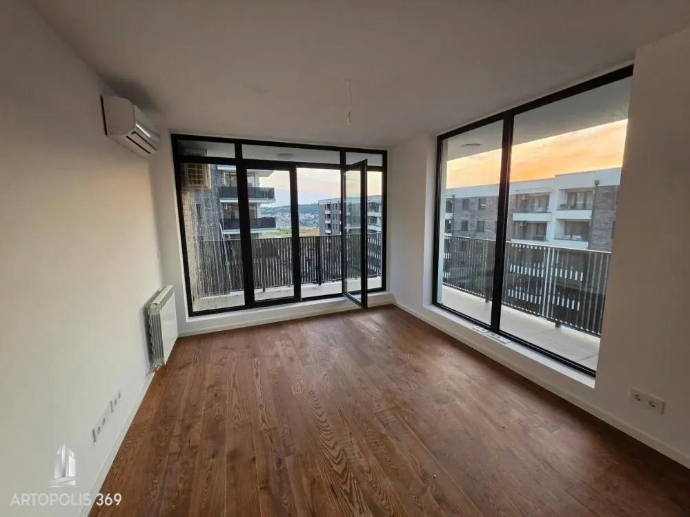 Empty room with wooden flooring, air conditioning and large glass surfaces leading to a terrace.