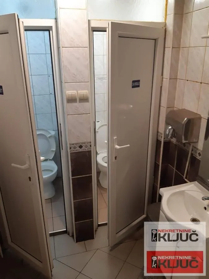 View of two toilets with white doors and a washbasin.