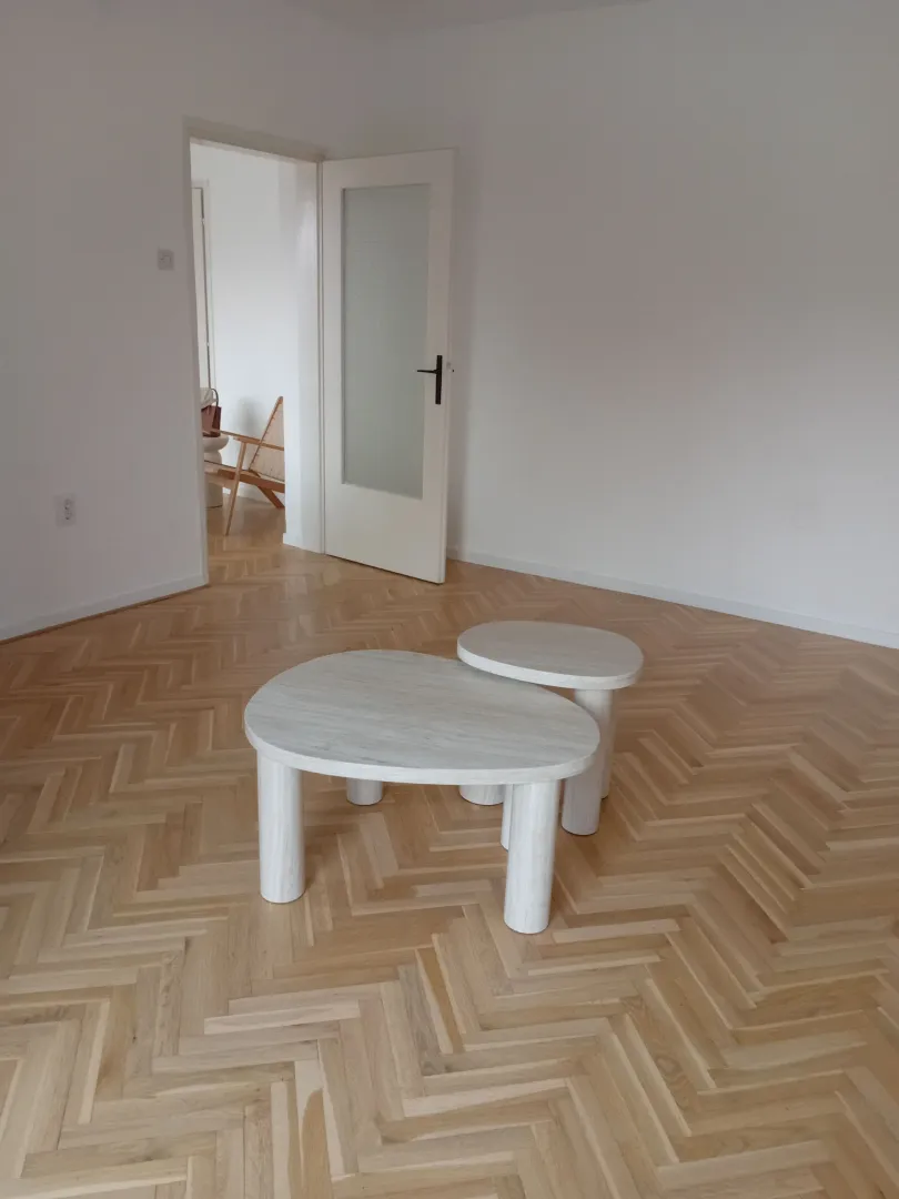 Svijetla prazna soba sa parketom i modernim stočićima.