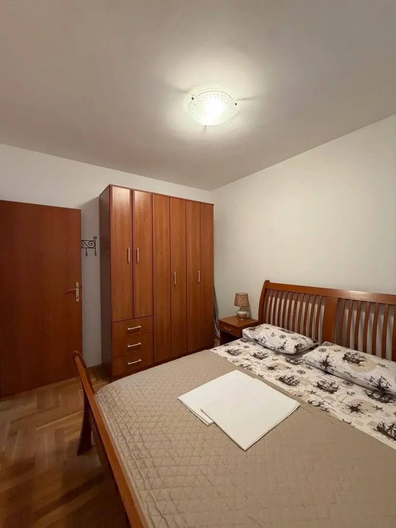 Namještena spavaća soba sa bračnim krevetom i drvenim ormarom.
