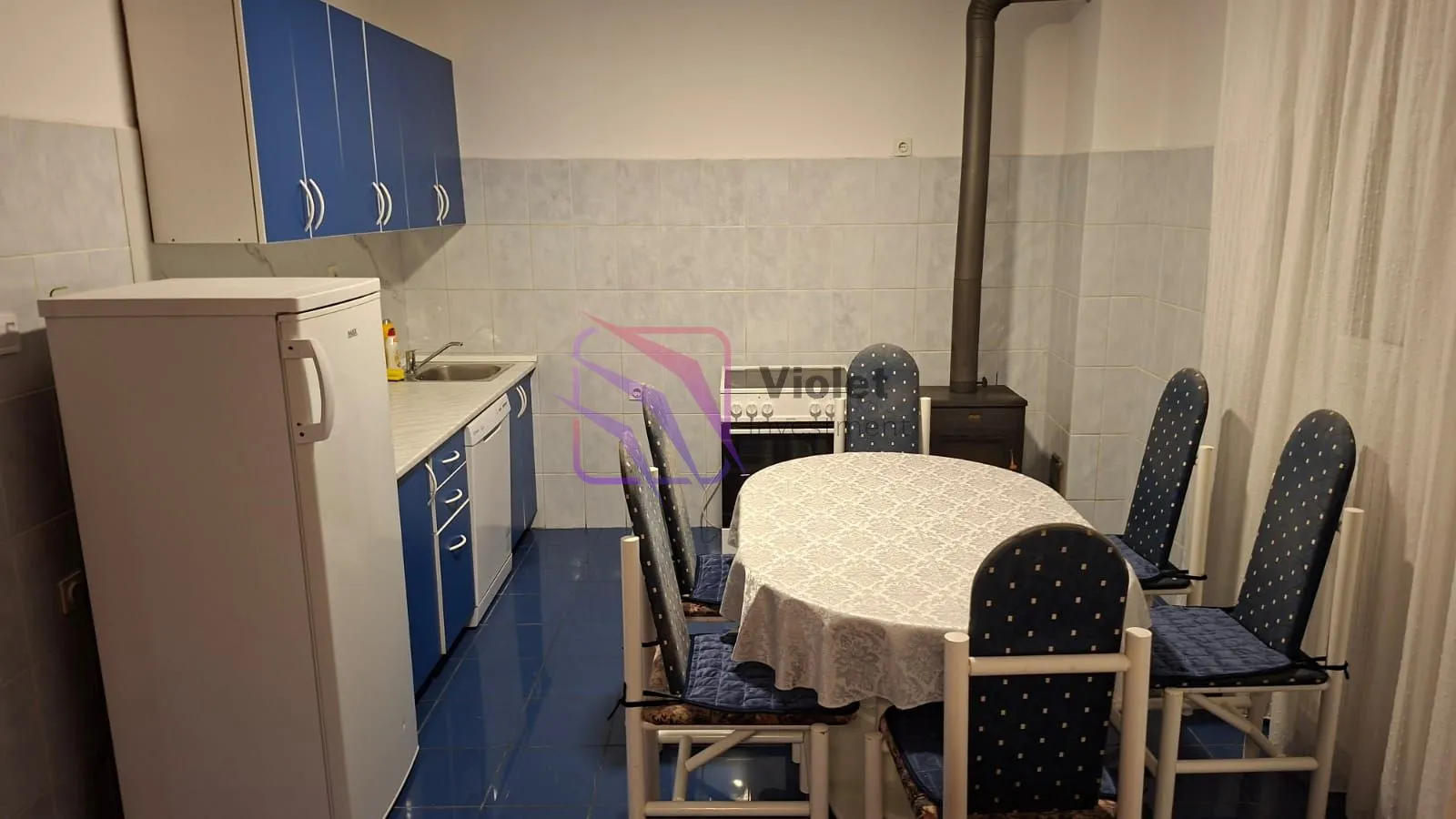 Kitchen with dining area equipped with blue cabinets, refrigerator, and a dining table with chairs.