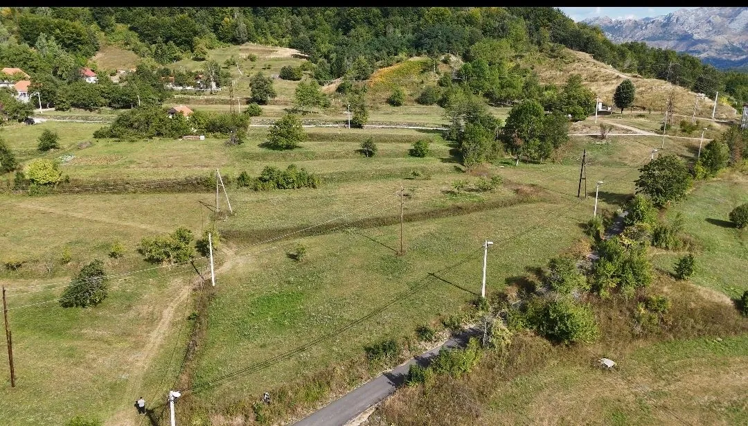 Pogled iz vazduha na prostrani seoski predio sa zelenim livadama i putem.