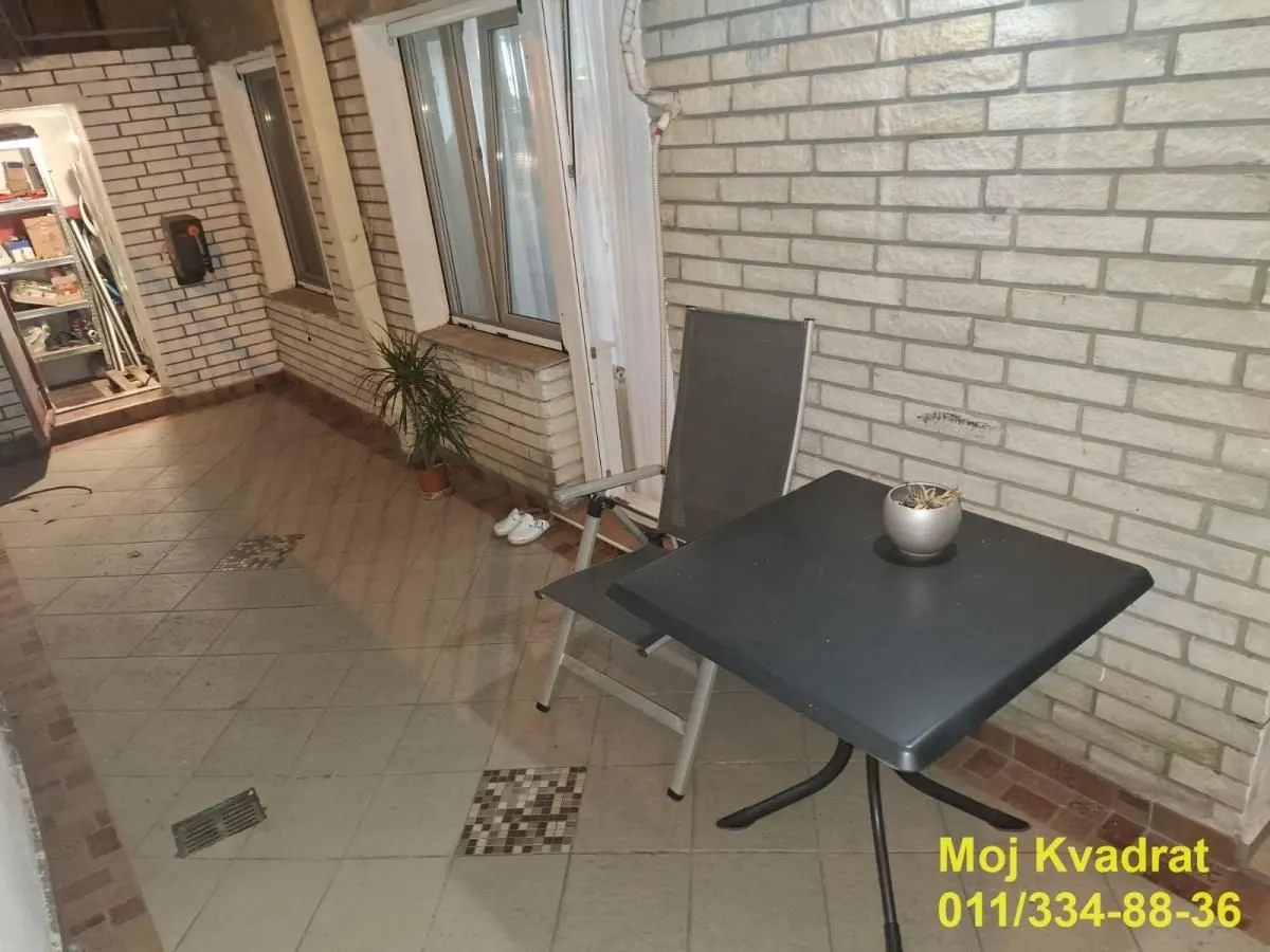 Natkrivena terasa sa stolom, stolicom i popločanim podom.