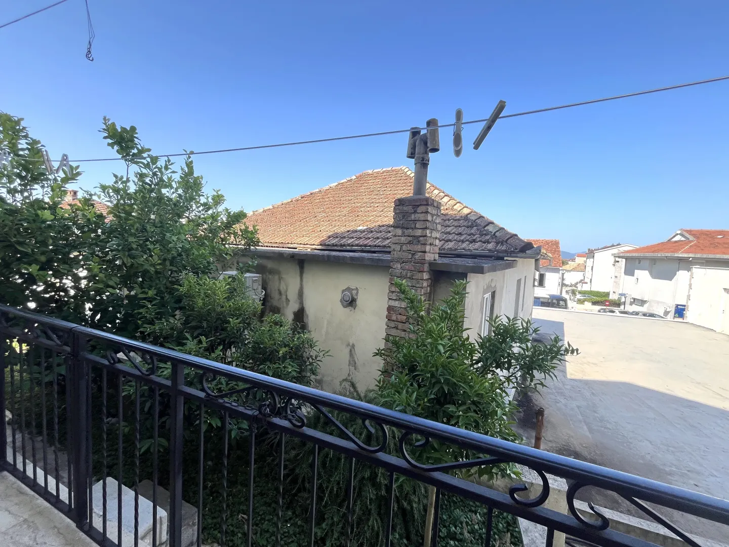 Pogled sa balkona na susjednu kuću i zelenilo pod vedrim nebom.