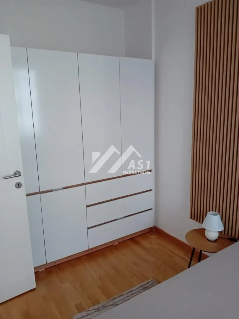 Spavaća soba sa velikim belim plakarom i drvenim panelima na zidu.