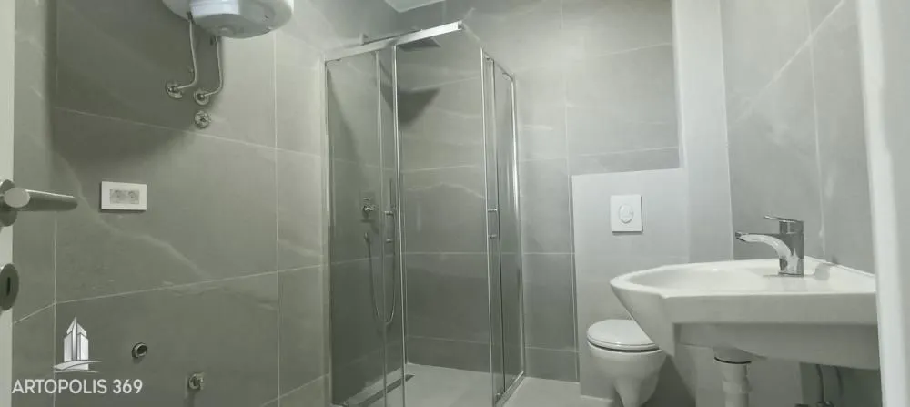 Moderno kupatilo sa tuš kabinom, umivaonikom i toaletom u sivoj keramici.