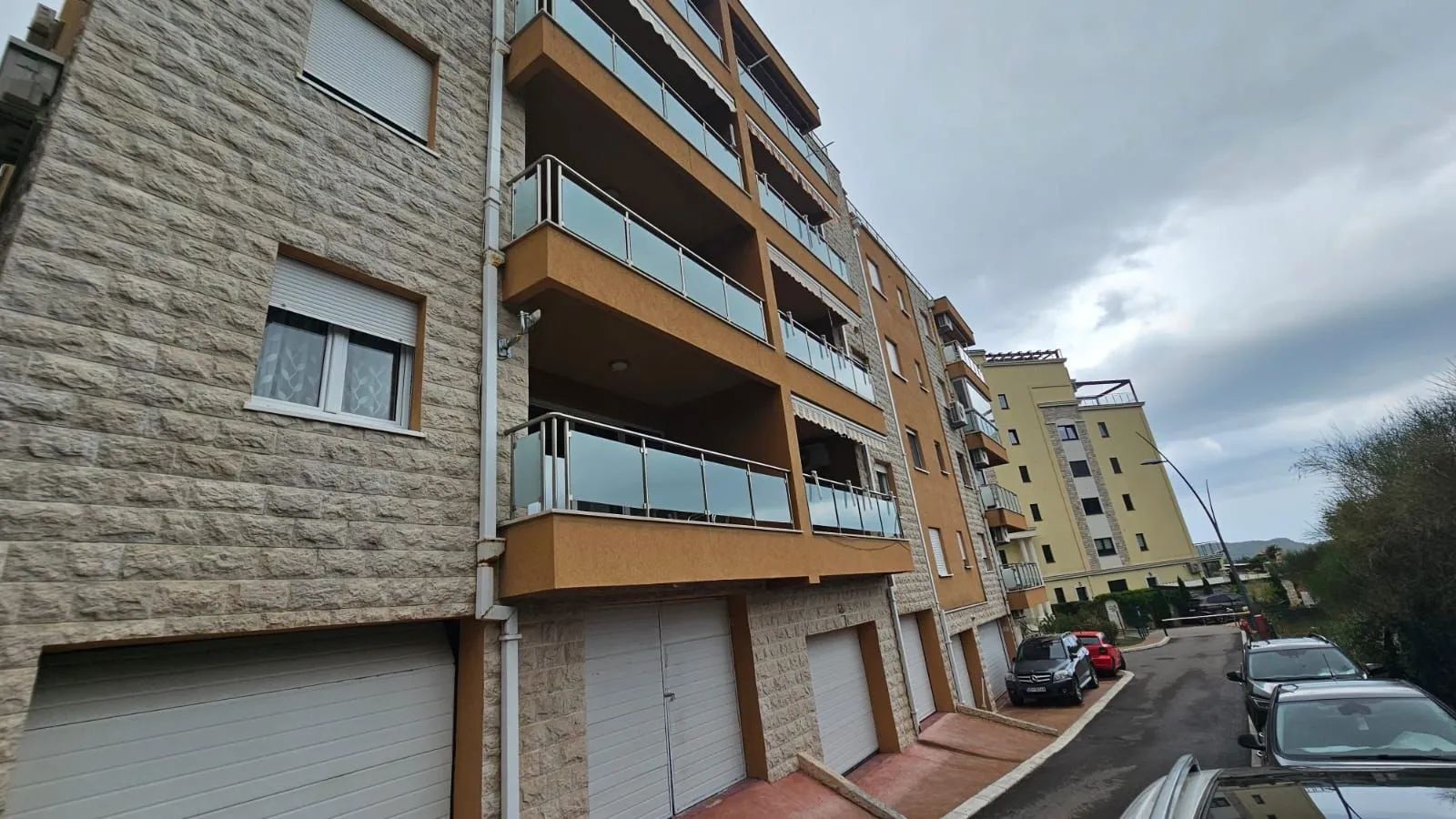 Spoljašnji izgled stambene zgrade sa terasama i garažama u prizemlju.
